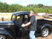 1971 Ford Ranchero - A man stands by a classic black pickup truck with its door open, while other vehicles are visible in the background.