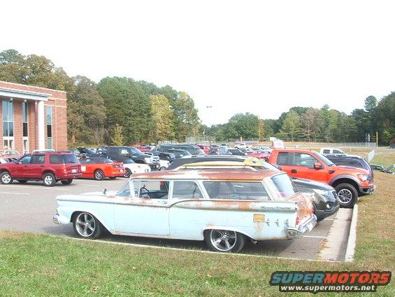 Light blue station wagon with surfboards on roof rack, parked in a lot with other vehicles