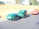 1971 Ford Ranchero - A green hot rod coupe tows a matching trailer, with a flatbed tow truck visible behind it.
