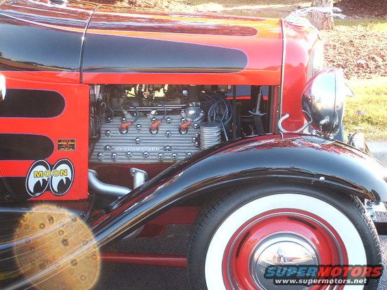 Exposed engine of a red and black hot rod with Moon eyes logo