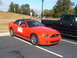 1971 Ford Ranchero - A bright orange convertible sports car is parked next to a black pickup truck in a parking lot.