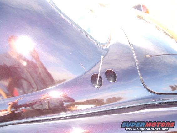 Close-up of a shiny purple car fender showing two circular holes and a reflection of the photographer