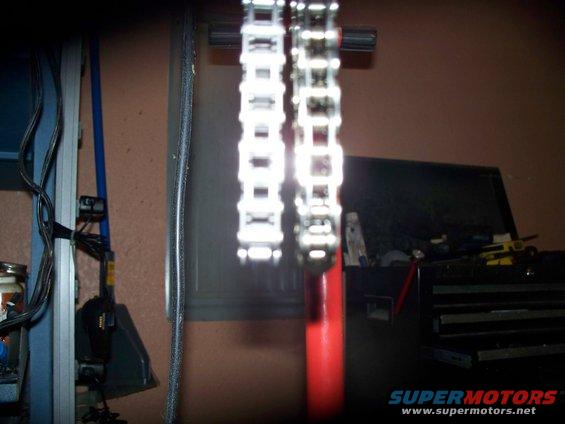 Close-up of two motorcycle timing chains, one brighter than the other, hanging vertically