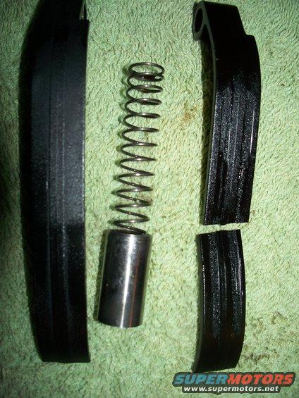 Motorcycle timing chain tensioner parts laid out on a green towel. Includes a spring, plunger, and two black plastic guides