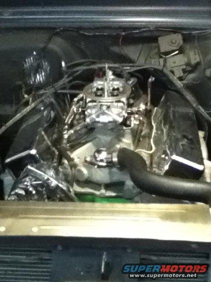 Engine bay with chrome carburetor and valve covers, black hoses, and visible wiring