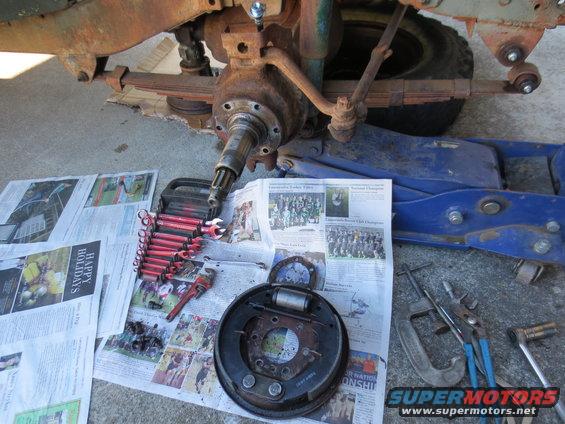 Rusty vehicle front axle assembly with brake drum and tools on newspaper