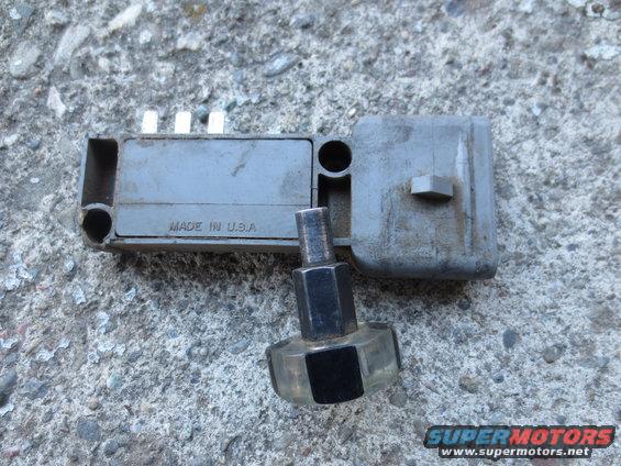 gray automotive ignition module with "MADE IN U.S.A." visible, resting on concrete