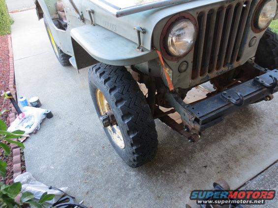 Light green Jeep Willys front end with rust on grille and bumper, showing a large tire and yellow rim