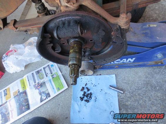 Disassembled vehicle brake drum, hub, and suspension components on the ground next to a blue hydraulic jack