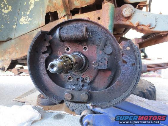 close-up of a rusty vehicle brake drum assembly with brake shoes and wheel cylinder visible, supported by a blue jack