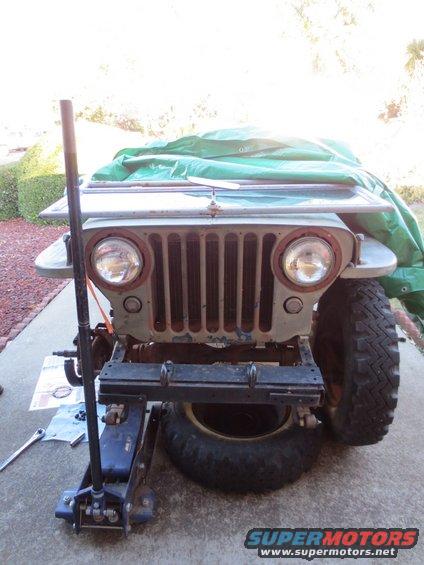 1946 Jeep CJ5 front end, partially covered, on a hydraulic jack with a spare tire underneath