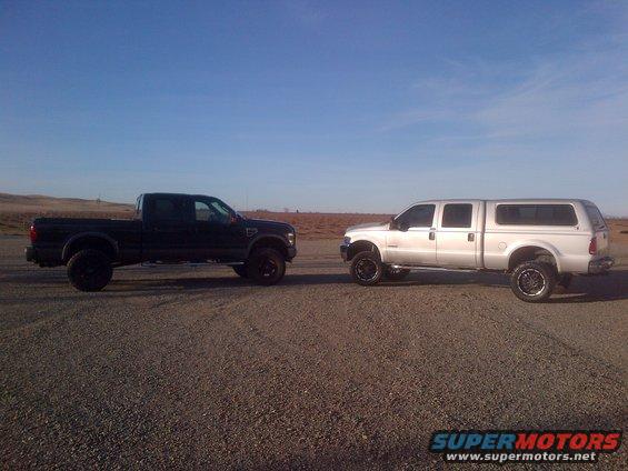 black pickup truck and silver pickup truck with camper shell parked on gravel lot