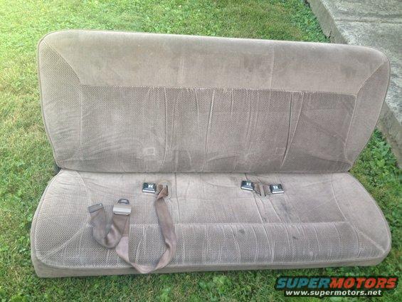 Brown fabric bench seat with seatbelts, sitting on grass