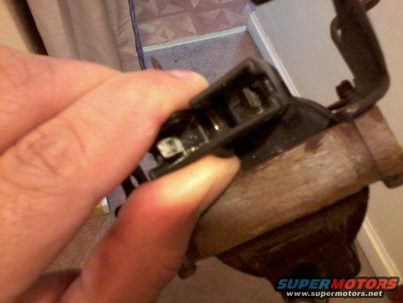 hand holding a black plastic electrical connector with wires attached to a metal part