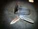 1984 BMW 3 Series - A folding knife and its sheath are displayed on a dark, textured surface.