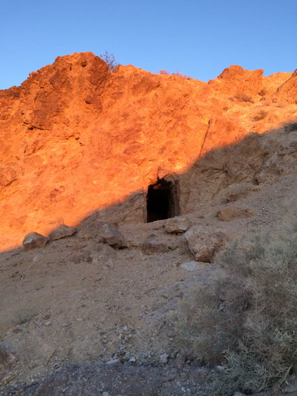 Cave entrance in a rocky hillside at sunset