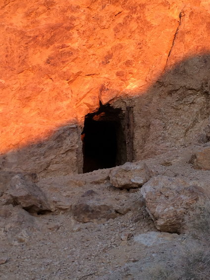 Entrance to a dark mine shaft in a rocky, sunlit hillside