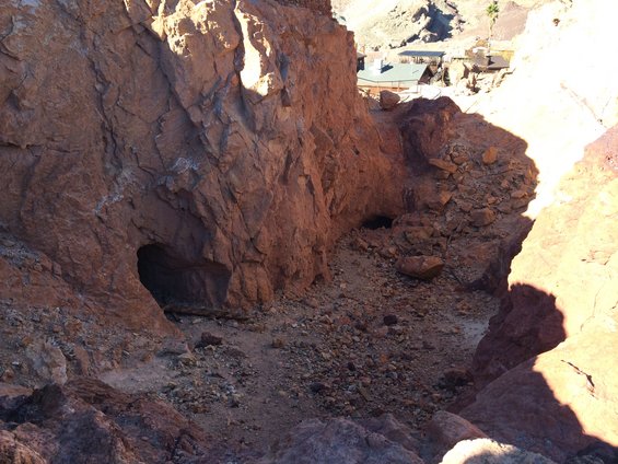 Rocky canyon with cave entrances and debris, buildings visible on a distant hillside
