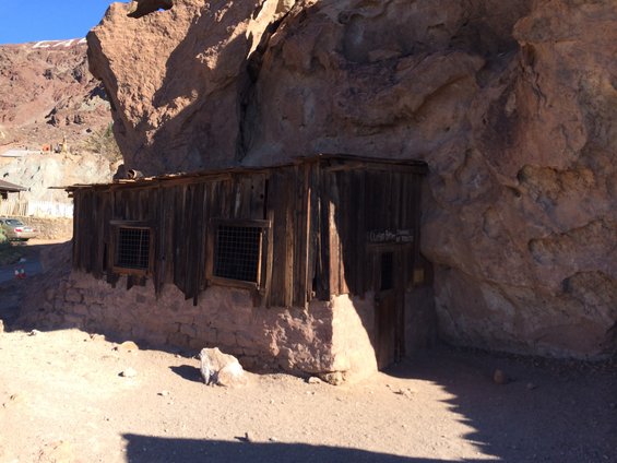 Old wooden building built into a rock face with barred windows