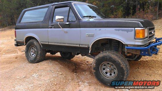 1990 Ford Bronco with aftermarket blue front bumper and off-road tires on dirt terrain