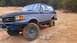 1990 Ford Bronco - A modified Ford Bronco navigates a challenging off-road terrain with its tires deep in the mud.