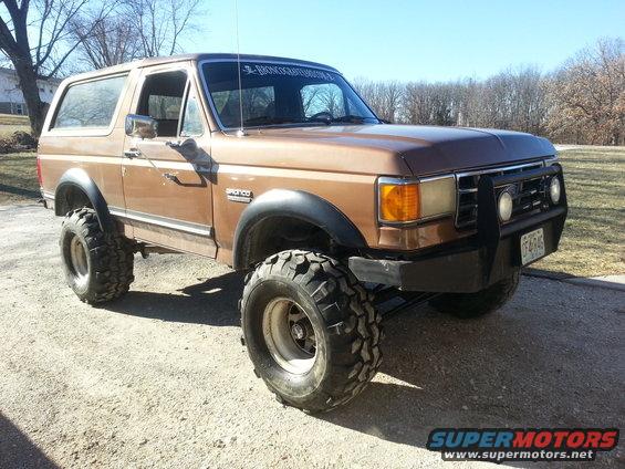 Brown 1987 Ford Bronco with lifted suspension and large off-road tires parked on a gravel surface