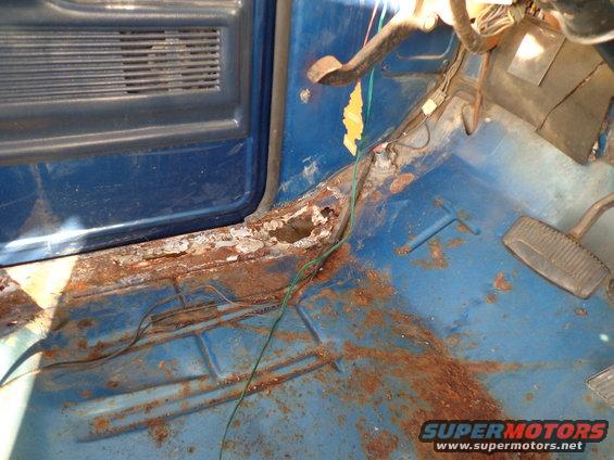 Interior floor and door jamb of a vehicle showing significant rust damage