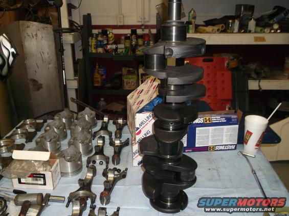engine crankshaft and pistons laid out on a table in a garage