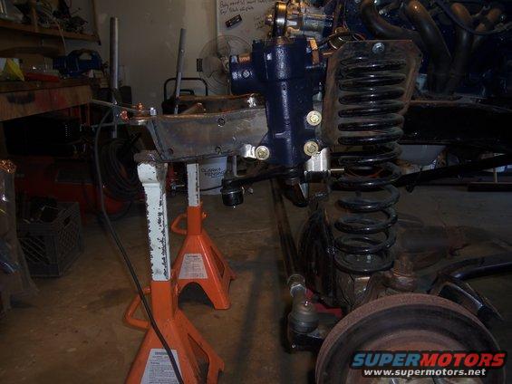 Vehicle suspension and steering parts on jack stands, showing a coil spring, steering box, and tie rod ends