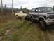 1970 Ford F-250 - Two Ford Broncos are stuck in a muddy, grassy area with trees and power lines in the background.