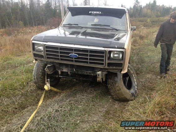 Ford truck with flat tire stuck in muddy field, tow strap attached to front bumper
