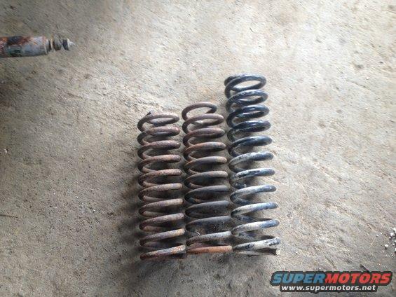 Three coil springs of varying sizes and a rusty shock absorber lie on a concrete surface