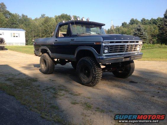 Dark blue and grey Ford Bronco with off-road tires and roof lights, parked on a dirt road