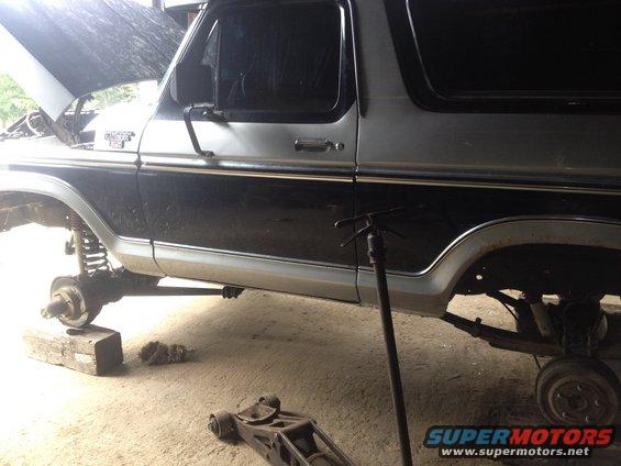 Side view of a two-tone Ford Bronco, hood up, wheels removed, on blocks