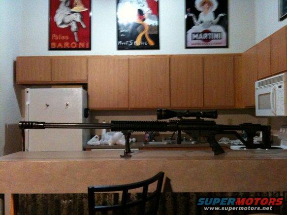 Sniper rifle with scope on a kitchen counter, with posters on the wall above