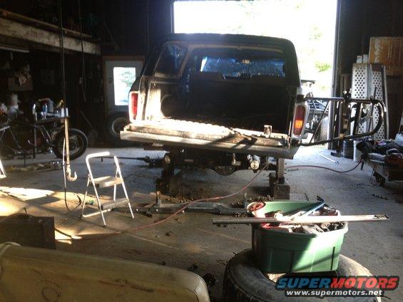 Pickup truck bed raised on jacks inside a garage, with a motorcycle and tools nearby