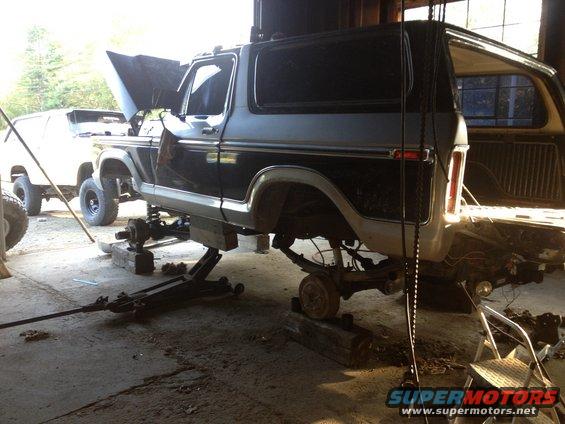 Black and gray Ford Bronco undergoing repairs, lifted on jacks with wheels removed