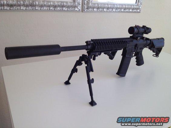 Assault rifle with suppressor, bipod, and scope on a white surface