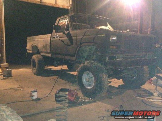 Dark-colored pickup truck with large tires, lifted suspension, and missing front bumper
