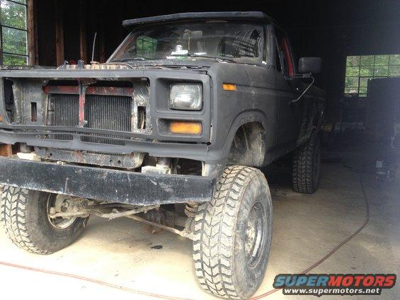 Front view of a matte black Ford pickup truck with its grille removed, parked indoors