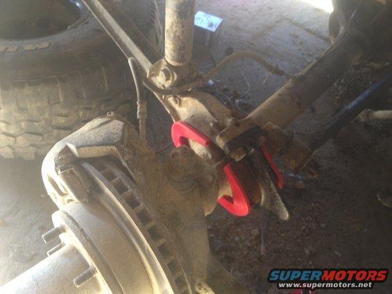 Red suspension part on a dirty vehicle axle with brake rotor visible