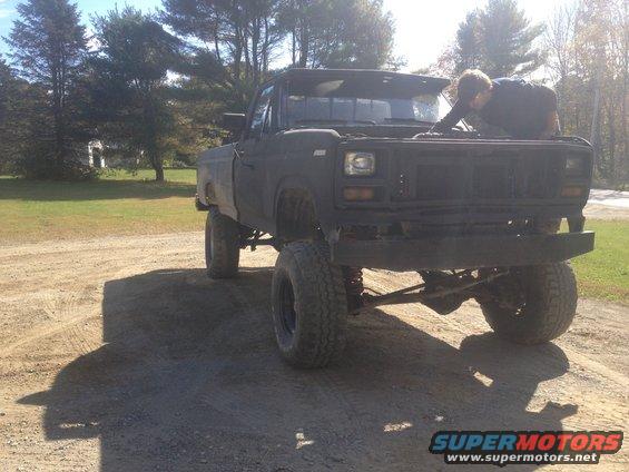 Black lifted pickup truck with hood open, person working on engine