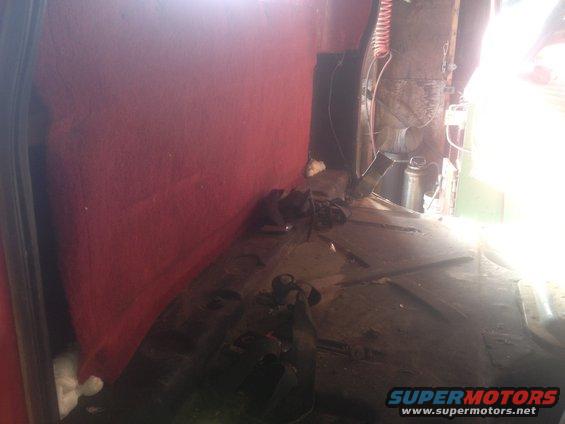 1970 Ford F-250 interior, red carpeted wall, dark floor with debris, bright light from rear