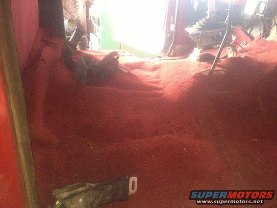 Interior shot of a vehicle's red carpeted floor and dashboard area, showing the gear shifter and seatbelt buckle