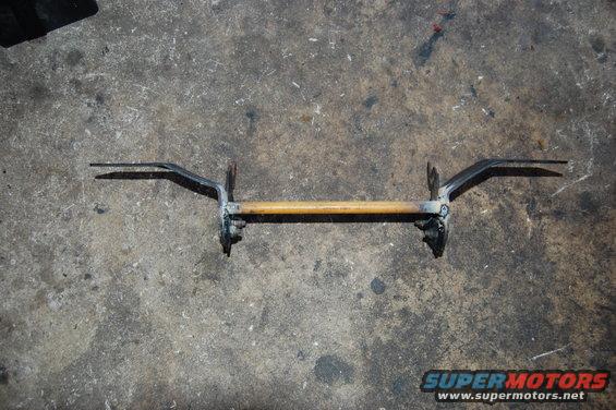 Metal bar with wooden handle and two pointed prongs, resting on concrete
