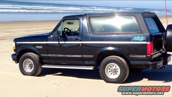 1992 Ford Bronco Nite edition parked on a sandy beach with the ocean in the background