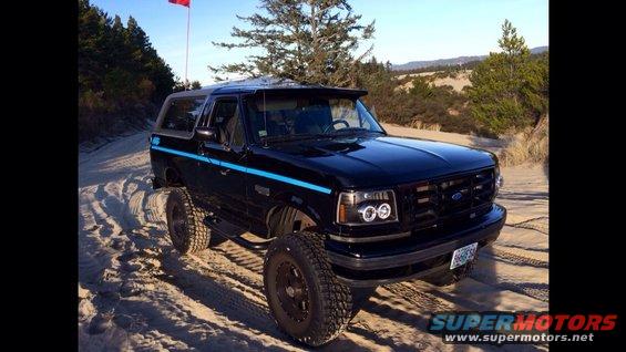 Black Ford Bronco on sandy terrain with a red flag on a pole behind it