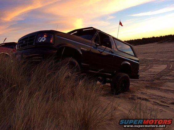 Black 1992 Ford Bronco on sand dunes with sunset sky