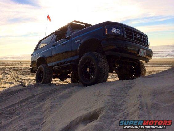 Black Ford Bronco driving on a sand dune near the ocean