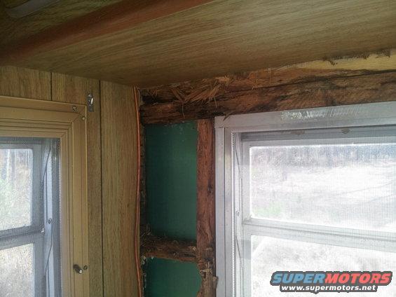 Interior view of a damaged wall with exposed wooden beams and insulation, next to a window